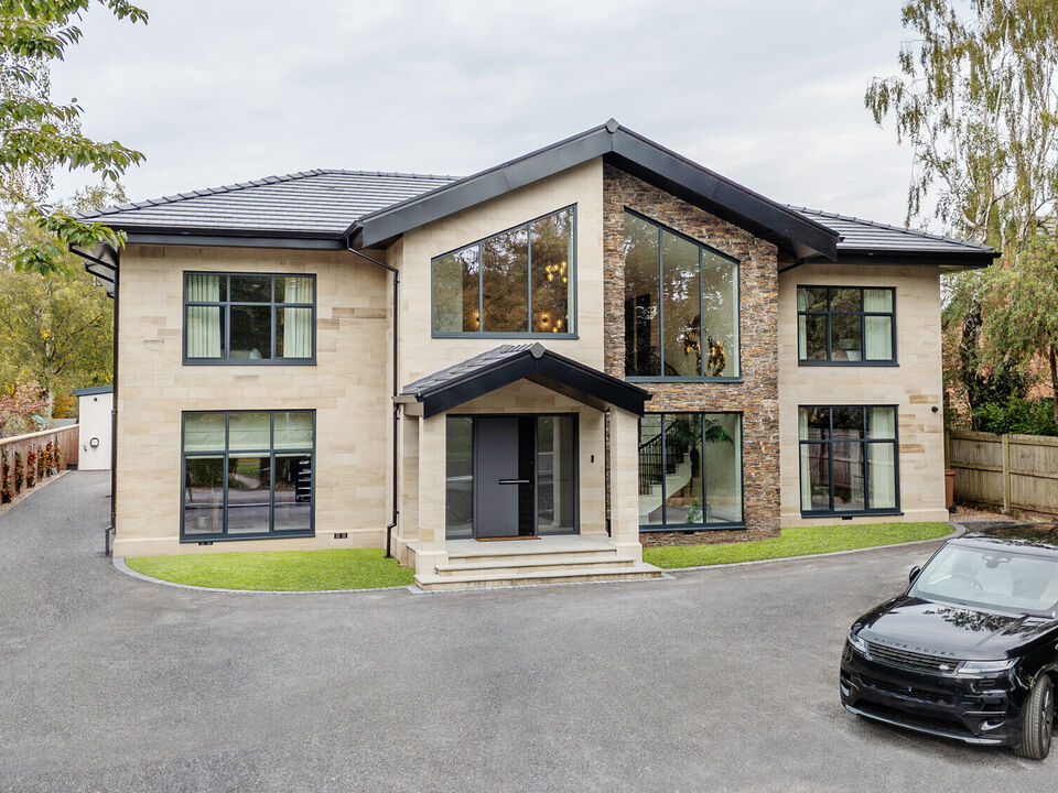Front elevation of a bespoke Cheshire residence featuring light ashlar stone masonry, dark grey window frames, and a modern gabled entrance.